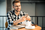 Happy young man holding smartphone in hands in cafe
