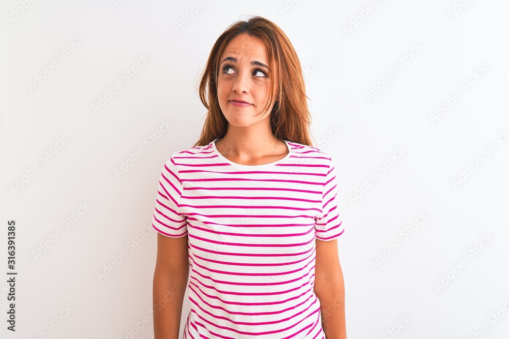 Young redhead woman wearing striped casual t-shirt stading over white isolated background smiling looking to the side and staring away thinking. Young redhead woman wearing striped casual t-shirt stading over white isolated background smiling looking to the side and staring away thinking.