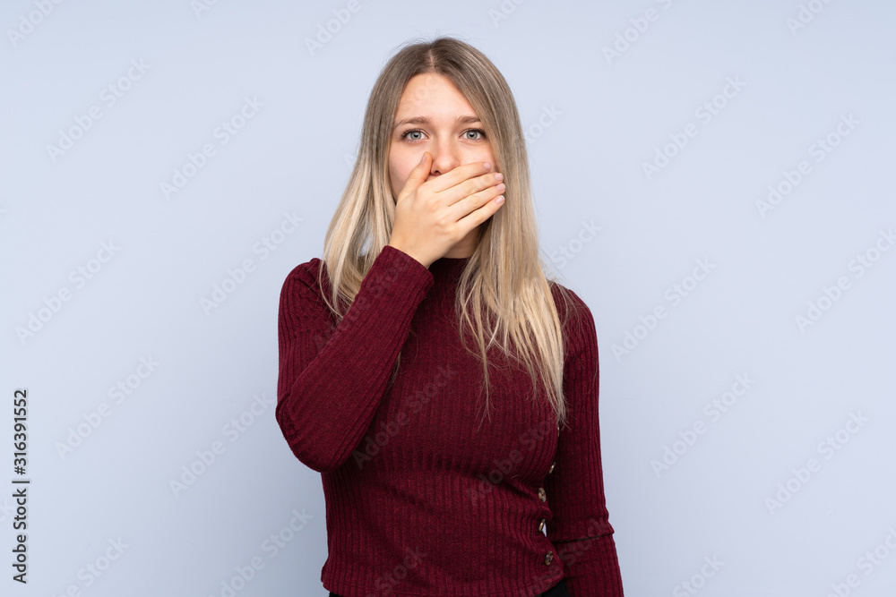Young blonde woman over isolated blue background covering mouth with hands Young blonde woman over isolated blue background covering mouth with hands