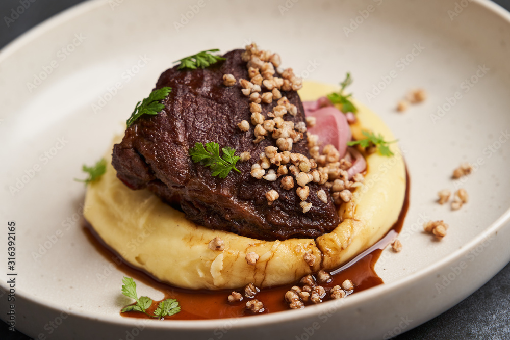 Stewed veal cheeks with mashed potatoes on a white plate, close-up. Stewed veal cheeks with mashed potatoes on a white plate, close-up.