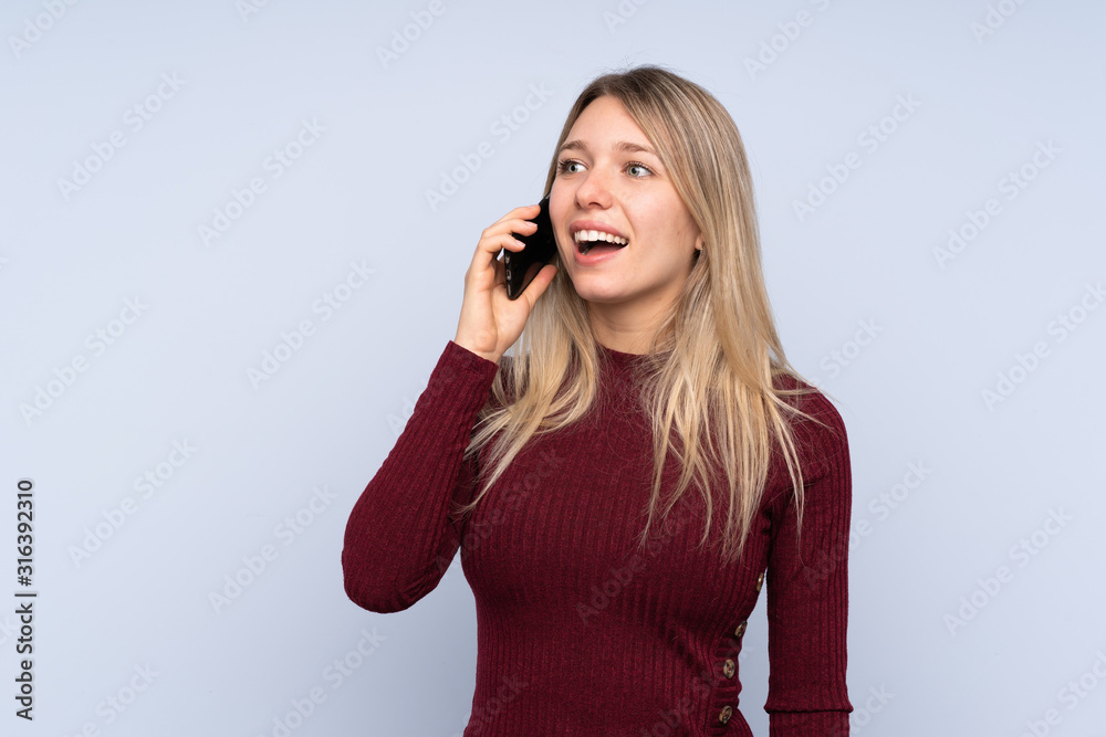 Young blonde woman over isolated blue background keeping a conversation with the mobile phone Young blonde woman over isolated blue background keeping a conversation with the mobile phone
