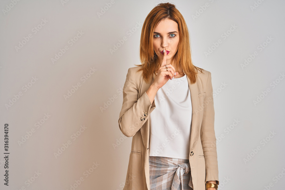 Redhead caucasian business woman standing over isolated background asking to be quiet with finger on lips. Silence and secret concept. Redhead caucasian business woman standing over isolated background asking to be quiet with finger on lips. Silence and secret concept.