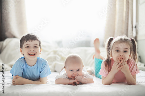 Children lie on the bed next to the newborn baby, little sister.