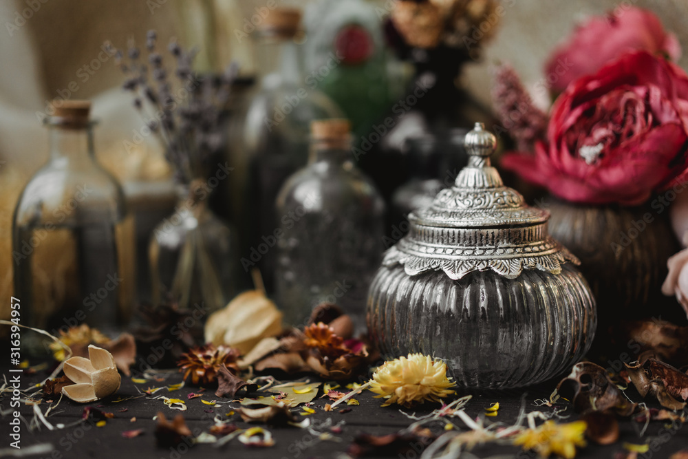 vintage jars, bottles, containers, flowers in smoke and dry leaves on a wooden table with warm light