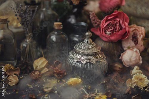 Fototapeta Naklejka Na Ścianę i Meble -  vintage jars, bottles, containers, flowers in smoke and dry leaves on a wooden table with warm light