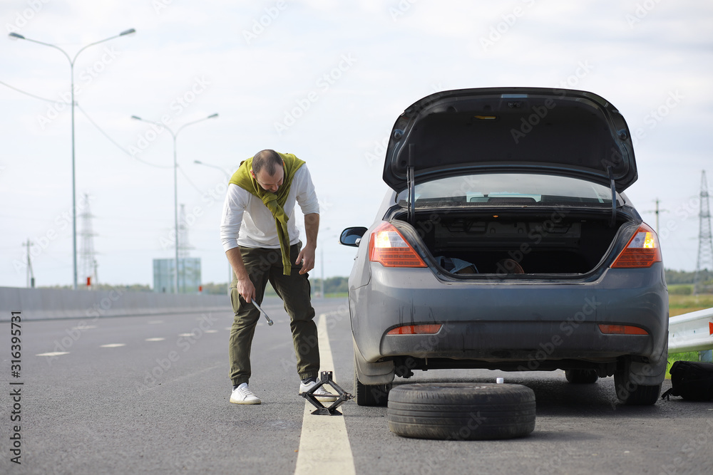 Replacing the wheel of a car on the road. A man doing tire work on the sidelines.