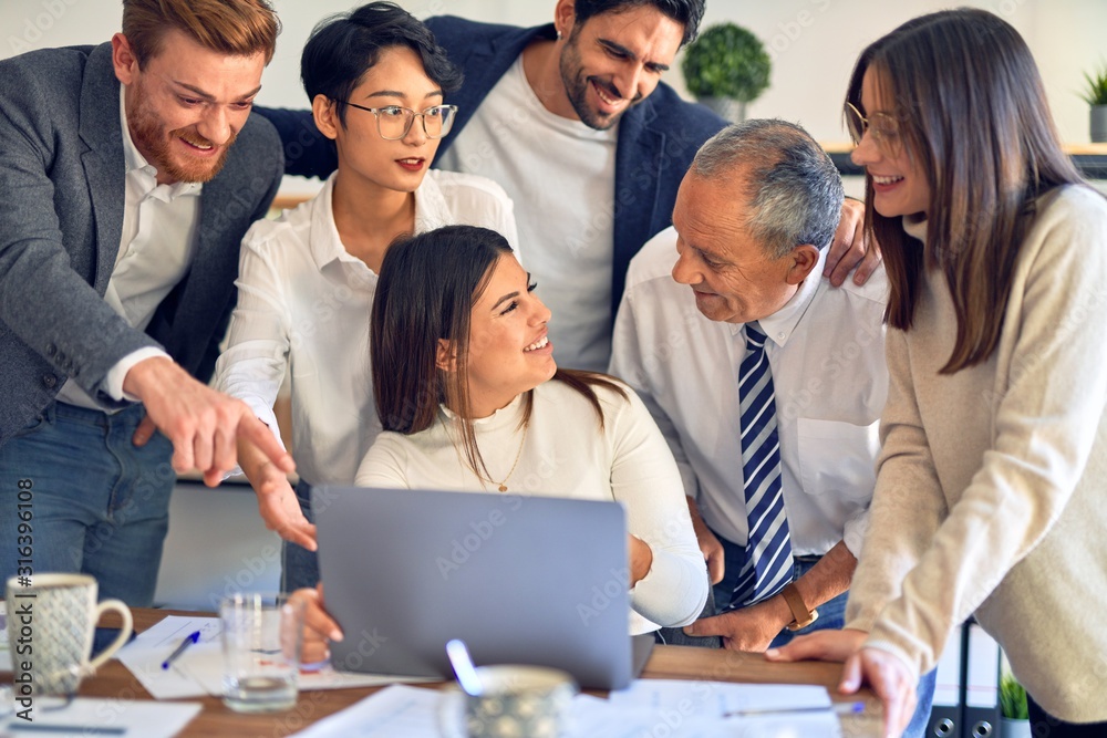 Fototapeta premium Group of business workers smiling happy and confident. One of them sitting and partners standing around. Working together with smile on face looking at the laptop at the office