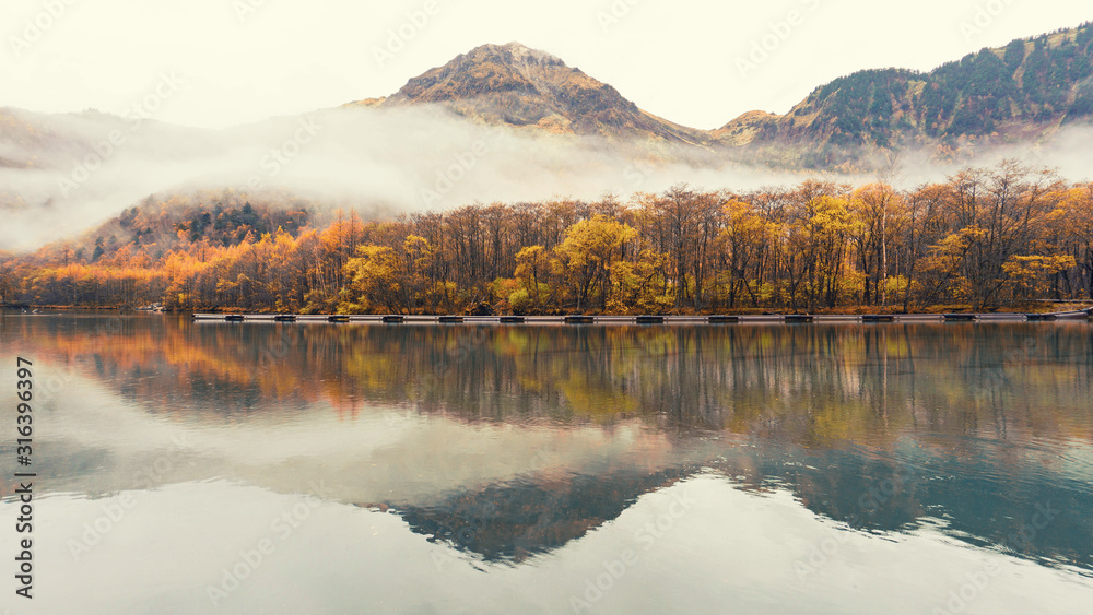 Autumn foliage season with green lake and mountains with many trees are blooming is background ,Kamikochi in Japan, Autumn concept.