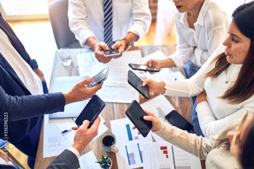 Group of business workers standing with hands together using smartphone doing symbol at the office