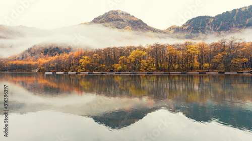 Autumn foliage season with green lake and mountains with many trees are blooming is background ,Kamikochi in Japan, Autumn concept.