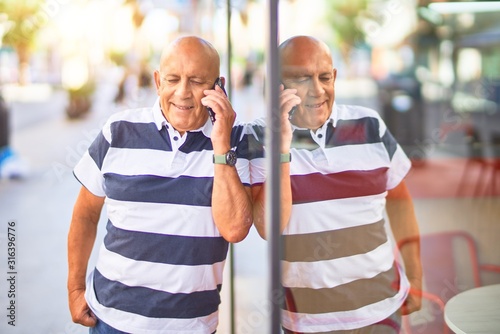 Senior handsome man smiling happy and confident. Leaning on the wall with smile on face talking by the smartphone at town street © Krakenimages.com