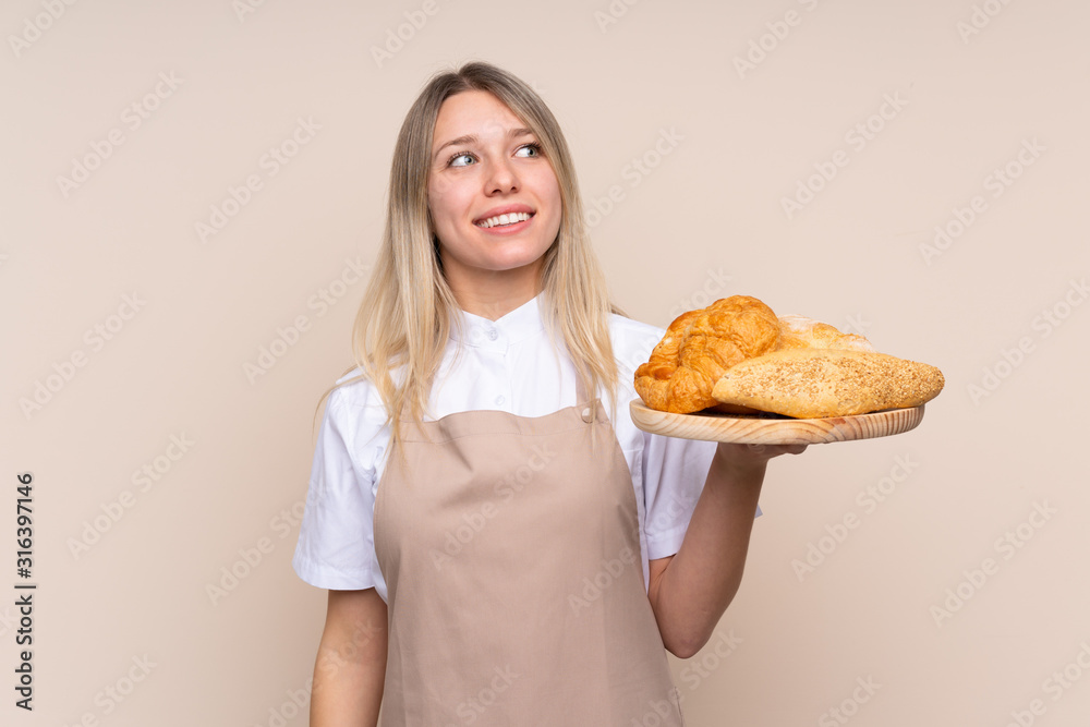 Young blonde girl with apron. Female baker holding a table with several breads looking up while smiling Young blonde girl with apron. Female baker holding a table with several breads looking up while smiling
