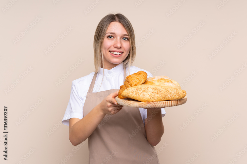Young blonde girl with apron. Female baker holding a table with several breads with happy expression Young blonde girl with apron. Female baker holding a table with several breads with happy expression