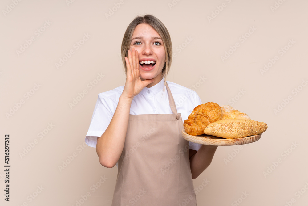 Young blonde girl with apron. Female baker holding a table with several breads shouting with mouth wide open Young blonde girl with apron. Female baker holding a table with several breads shouting with mouth wide open