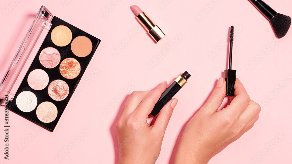 Woman hands holding open black mascara on pastel pink background, top view. Minimal beauty background with makeup products, flat lay, copy space. Eye and face make up concept Woman hands holding open black mascara on pastel pink background, top view. Minimal beauty background with makeup products, flat lay, copy space. Eye and face make up concept