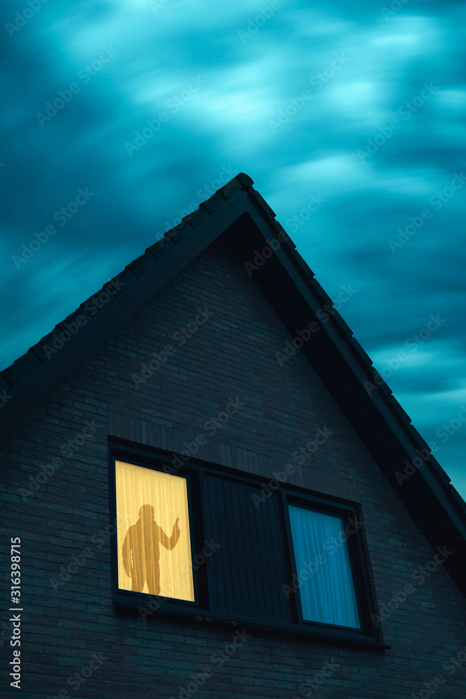 Burglar with handgun in ominous house with illuminated window under stormy sky at dusk.