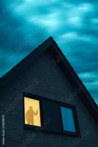 Burglar with handgun in ominous house with illuminated window under stormy sky at dusk. © ysbrandcosijn