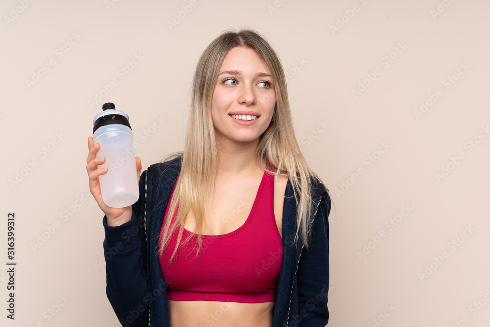 Young sport blonde woman over isolated background with sports water bottle Young sport blonde woman over isolated background with sports water bottle