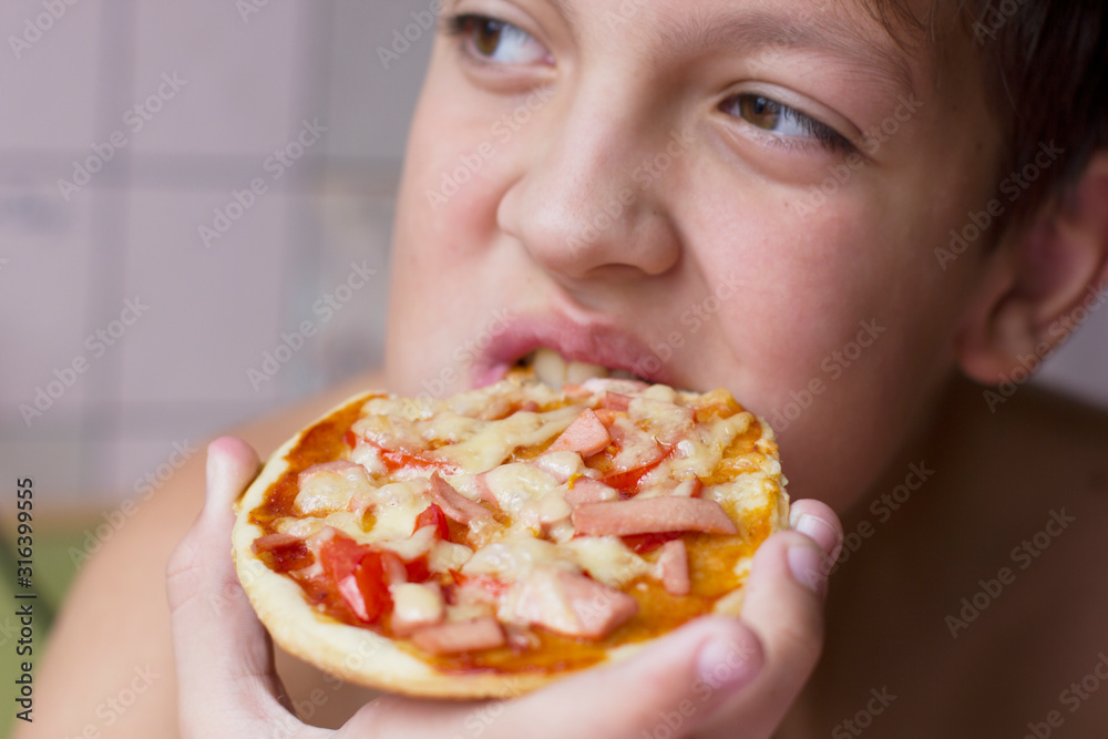 Boy eating pizza at home in the kitchen