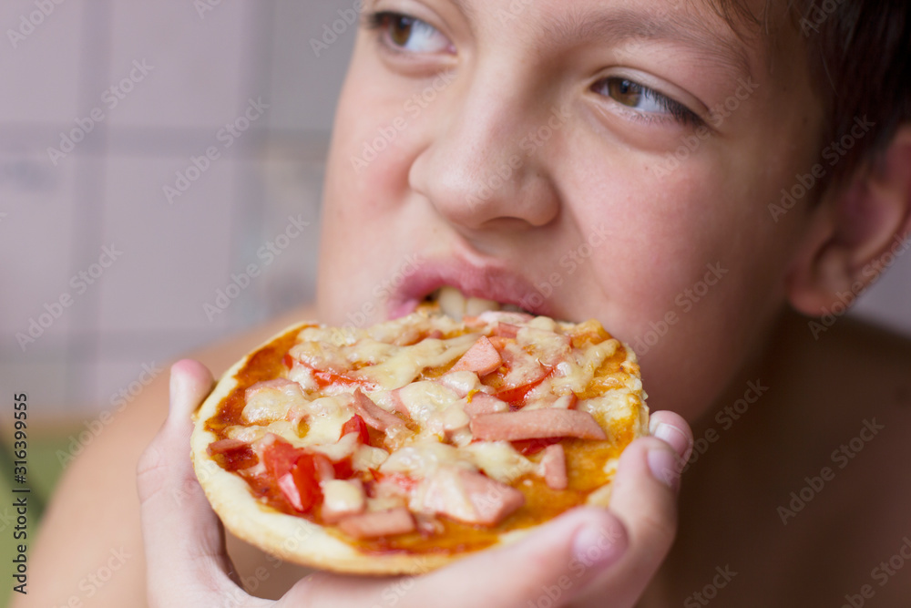 Boy eating pizza at home in the kitchen Boy eating pizza at home in the kitchen