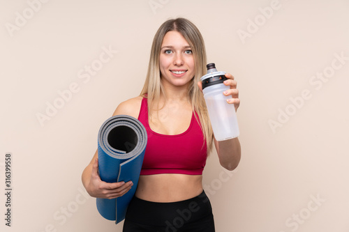 Young sport blonde woman over isolated background with sports water bottle and with a mat