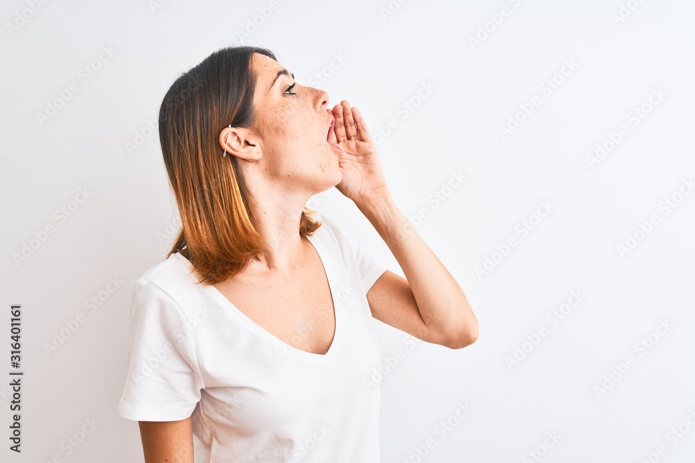 Beautiful redhead woman wearing casual white t-shirt over isolated background shouting and screaming loud to side with hand on mouth. Communication concept. Beautiful redhead woman wearing casual white t-shirt over isolated background shouting and screaming loud to side with hand on mouth. Communication concept.