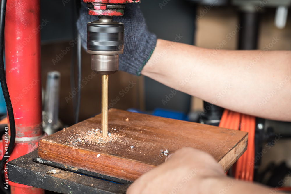 hand of worker man holding Electric drilling machine on wooden with Drill Press machine . selective focus