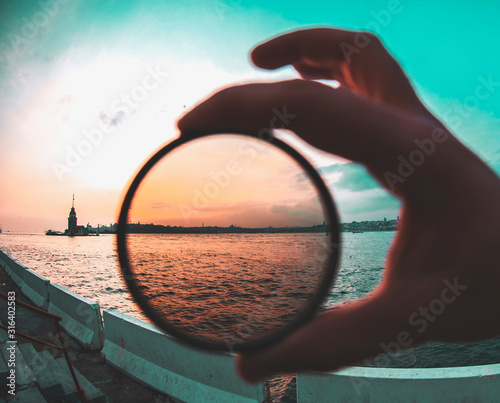 Fotografi a man holding a photo filter with backgorund of Maiden Tower during sunset