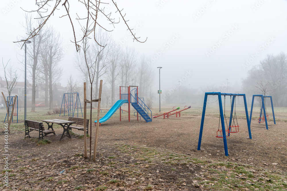 Novi Sad, Serbia - January 16, 2020: Children's playground with fog. Empty playground with carousels and swings in misty park.