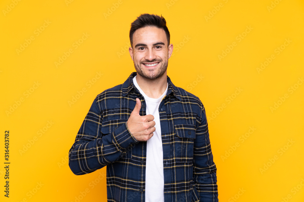 Young handsome man over isolated yellow background giving a thumbs up gesture Young handsome man over isolated yellow background giving a thumbs up gesture