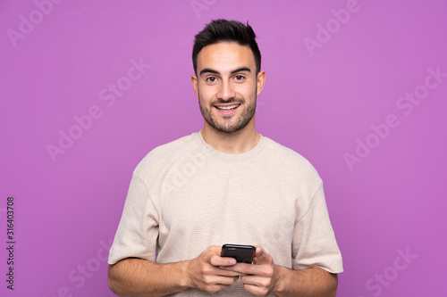 Young handsome man over isolated purple background surprised and sending a message © luismolinero