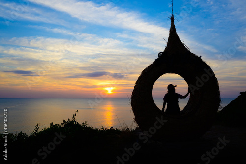 Siluate women sit down on  giant bird nest at the beach before sunset  
