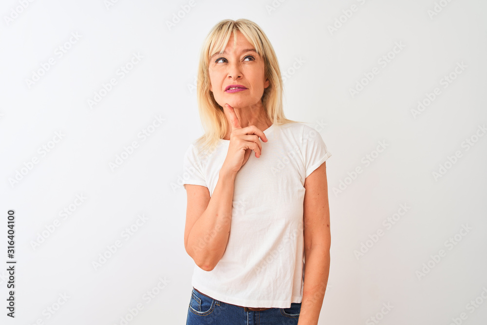 Middle age woman wearing casual t-shirt standing over isolated white background Thinking concentrated about doubt with finger on chin and looking up wondering Middle age woman wearing casual t-shirt standing over isolated white background Thinking concentrated about doubt with finger on chin and looking up wondering