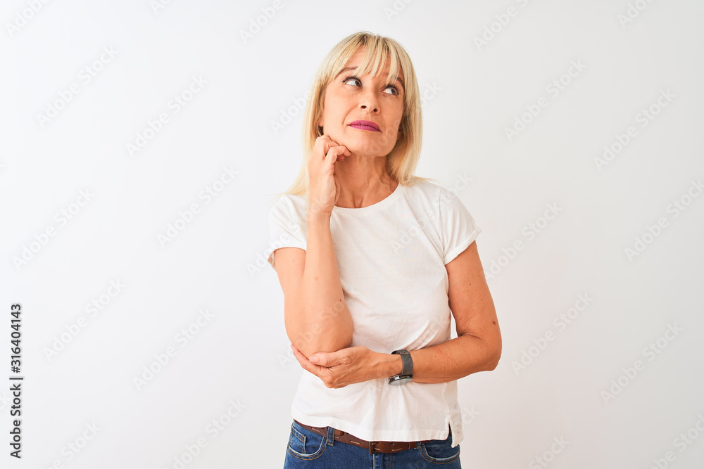 Middle age woman wearing casual t-shirt standing over isolated white background with hand on chin thinking about question, pensive expression. Smiling with thoughtful face. Doubt concept. Middle age woman wearing casual t-shirt standing over isolated white background with hand on chin thinking about question, pensive expression. Smiling with thoughtful face. Doubt concept.
