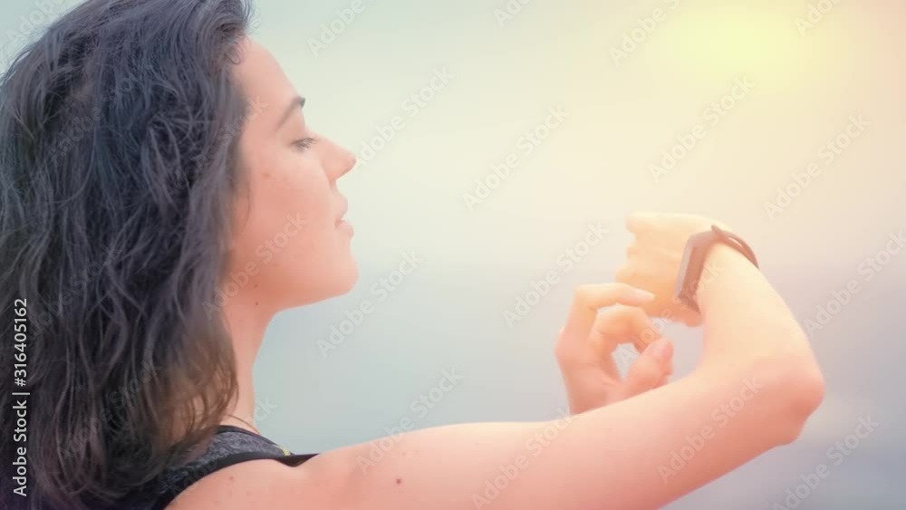 Woman jogger in sport clothes on the seashore looking data on fitness watch Woman jogger in sport clothes on the seashore looking data on fitness watch