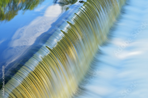 Landscape of the Battle Creek River cascade captured with motion blur and with reflections of trees and clouds in calm water, Michigan, USA photo