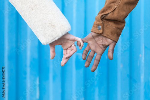 Arms of interracial couple holding hands, great love symbolic concept, blue background.