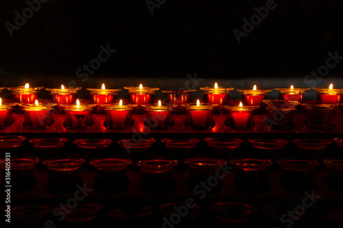 A row of many bright burning candles in the dark. Close-up. Space for text.