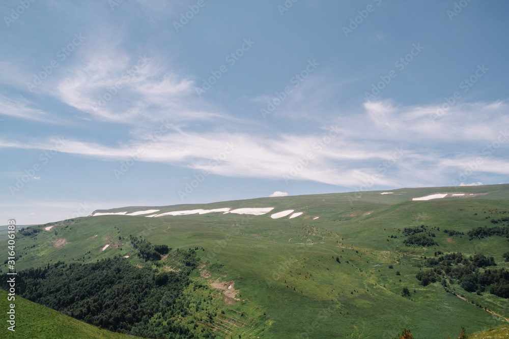 Fototapeta premium Summer view of the plateau lago naki with snow. Beautiful clouds and mountain in a blue haze.