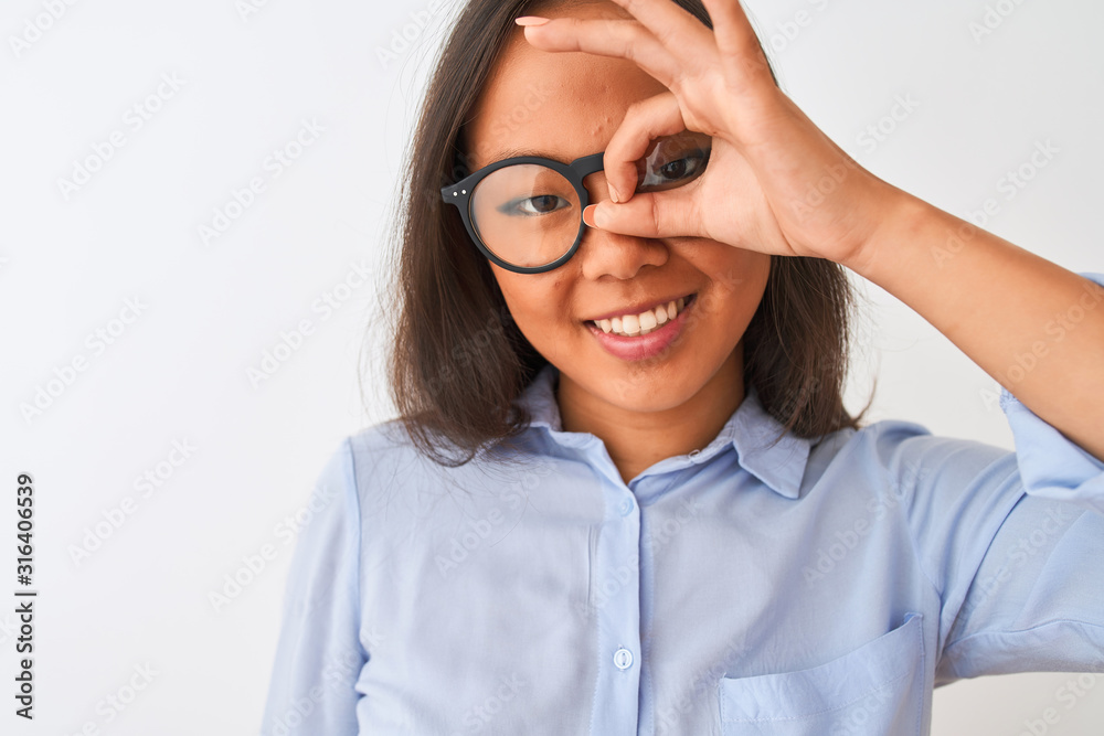 Obraz premium Young chinese woman wearing shirt and glasses standing over isolated white background with happy face smiling doing ok sign with hand on eye looking through fingers
