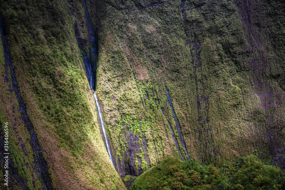 Aerial view of Kauai's lush colorful interior mountain landscape. Weeping waterfalls dot the landscape. 