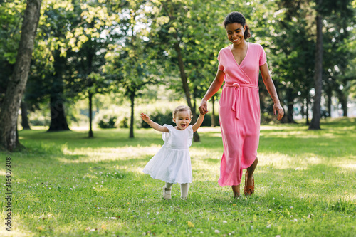 Young mother and her happy daughter run in the park 