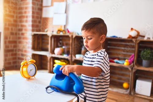 Beautiful toddler boy playing with vintage blue phone at kindergarten