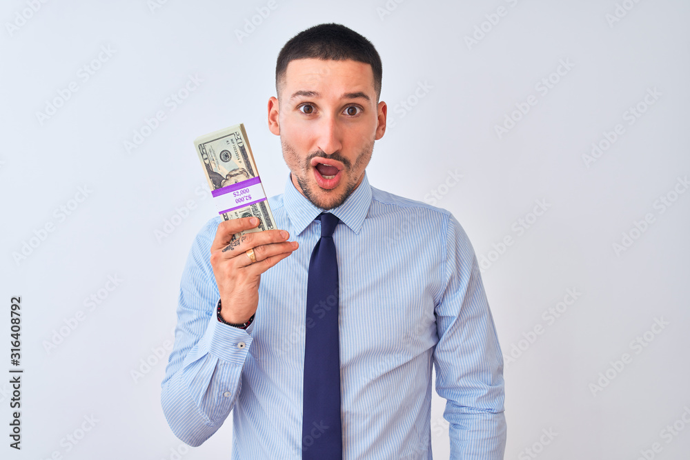 Young handsome business man holding a bunch of dollars bank notes over isolated background scared in shock with a surprise face, afraid and excited with fear expression Young handsome business man holding a bunch of dollars bank notes over isolated background scared in shock with a surprise face, afraid and excited with fear expression