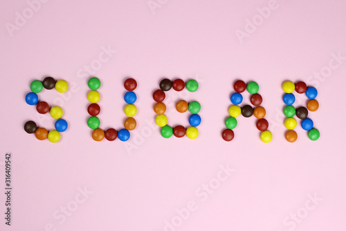 The word Sugar from colored candies on a pink background