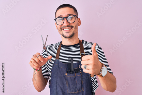 Young handsome hairdresser man wearing apron over pink isolated background happy with big smile doing ok sign, thumb up with fingers, excellent sign