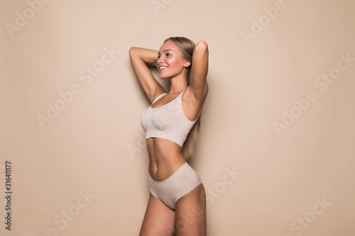 Young pretty woman standing in beige lingerie isolated on beige background