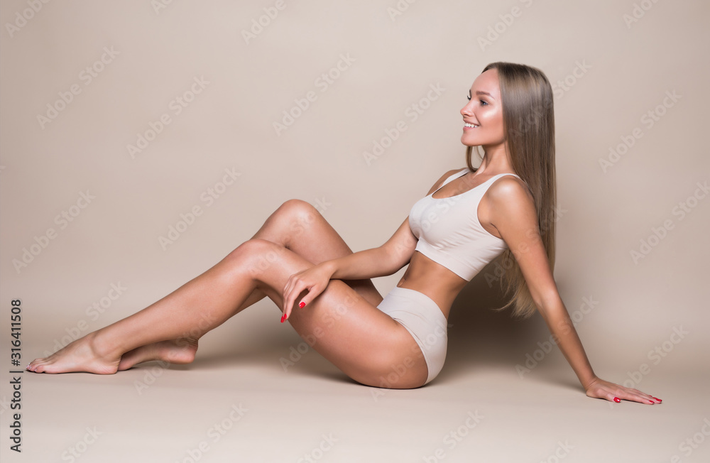 Side view photo of the tender pretty young woman with a charming smile lying on the floor isolated on beige background Side view photo of the tender pretty young woman with a charming smile lying on the floor isolated on beige background