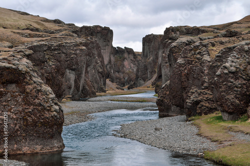 A trickling stream cuts through the mighty, snaking Fjadrargljufur Canyon on a moody summer day. The volcanic rock is typical of the area - South East Iceland