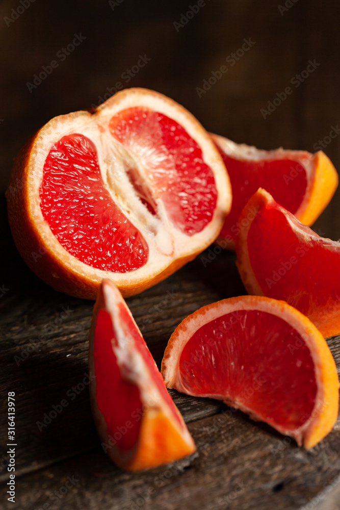 Slices of ripe fresh organic grapefruit on a rustic wooden board. Natural source of vitamins, low calories tasty dessert. Dark background, close up, front view Slices of ripe fresh organic grapefruit on a rustic wooden board. Natural source of vitamins, low calories tasty dessert. Dark background, close up, front view
